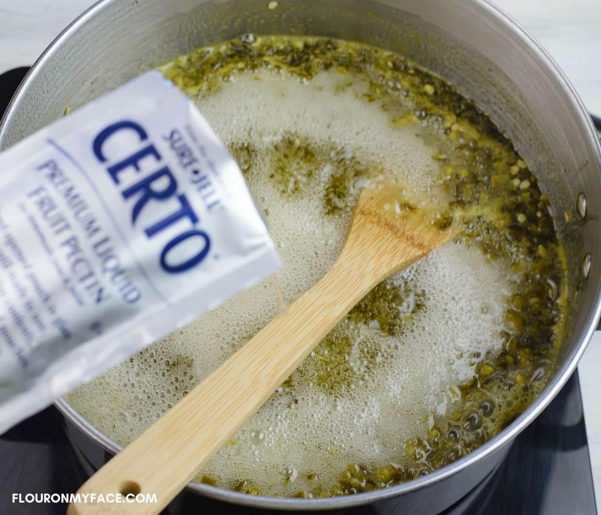 Adding liquid pectin to a pot of jalapeno jelly that has reached the rolling boil stage.