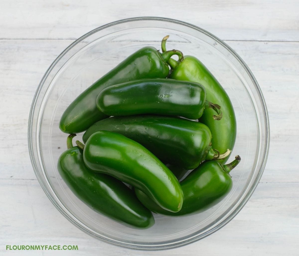 A glass bowl filled with fresh jalapeno peppers.