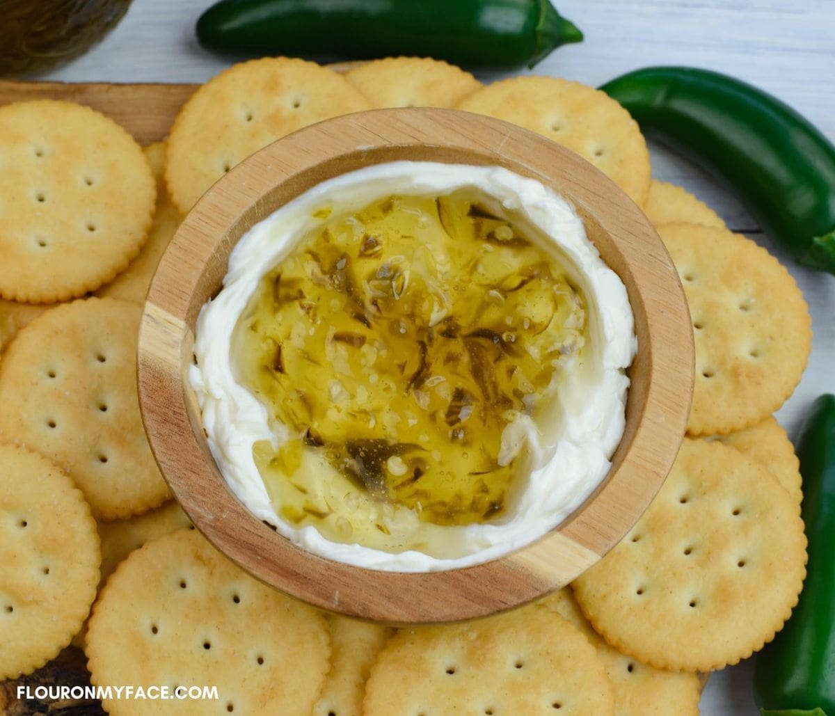 A wooden bowl filled with cream cheese and pepper jelly with crackers around the bowl.