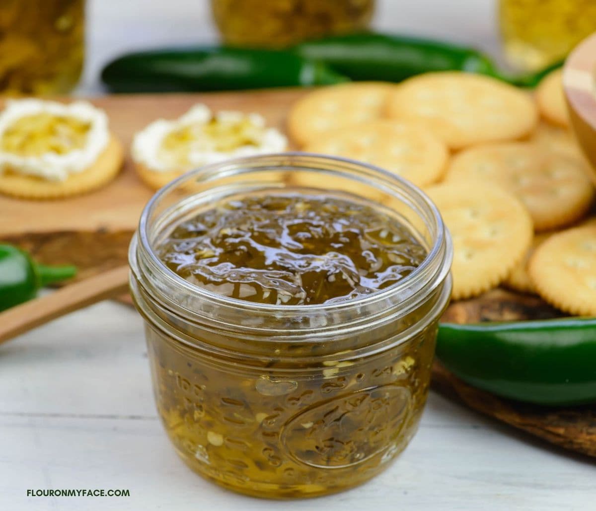 Jalapeno jelly in an opened canning jar with crackers and cream cheese in the background.