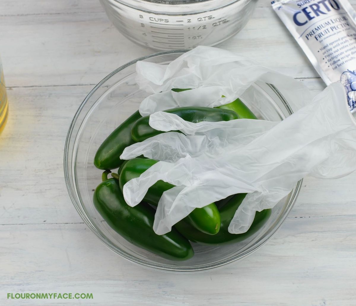 Jalapeno peppers in a bowl with a pair of plastic gloves for protection.