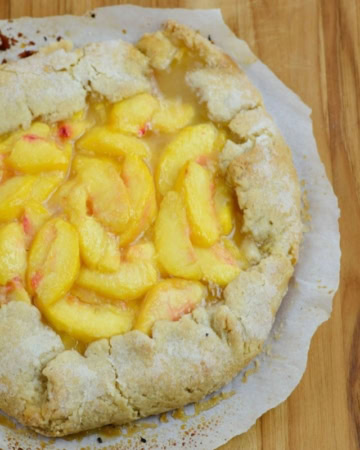 A freshly baked peach galette on a wooden cutting board.