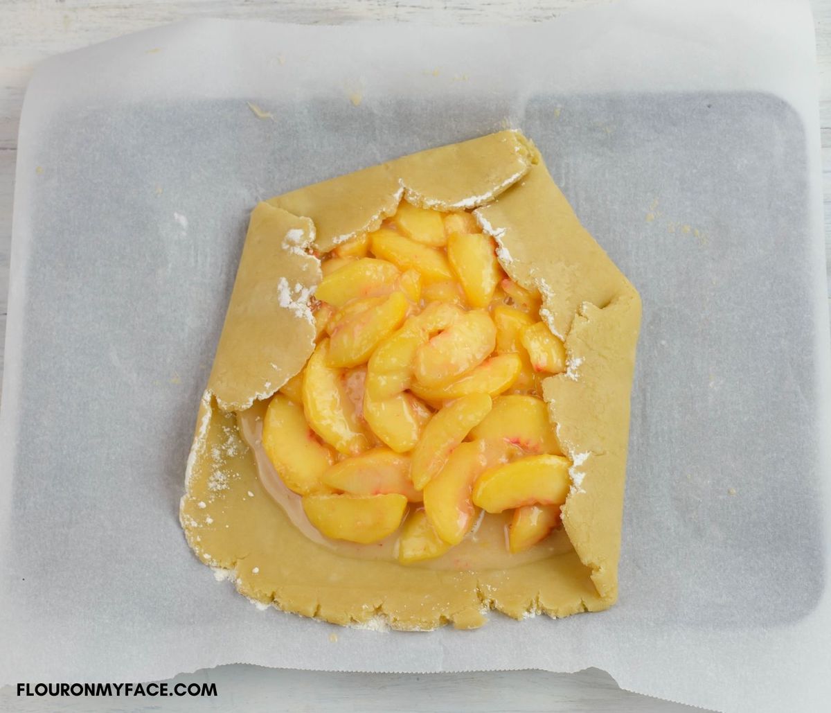 Folding the crust for a peach Galette over the filling.