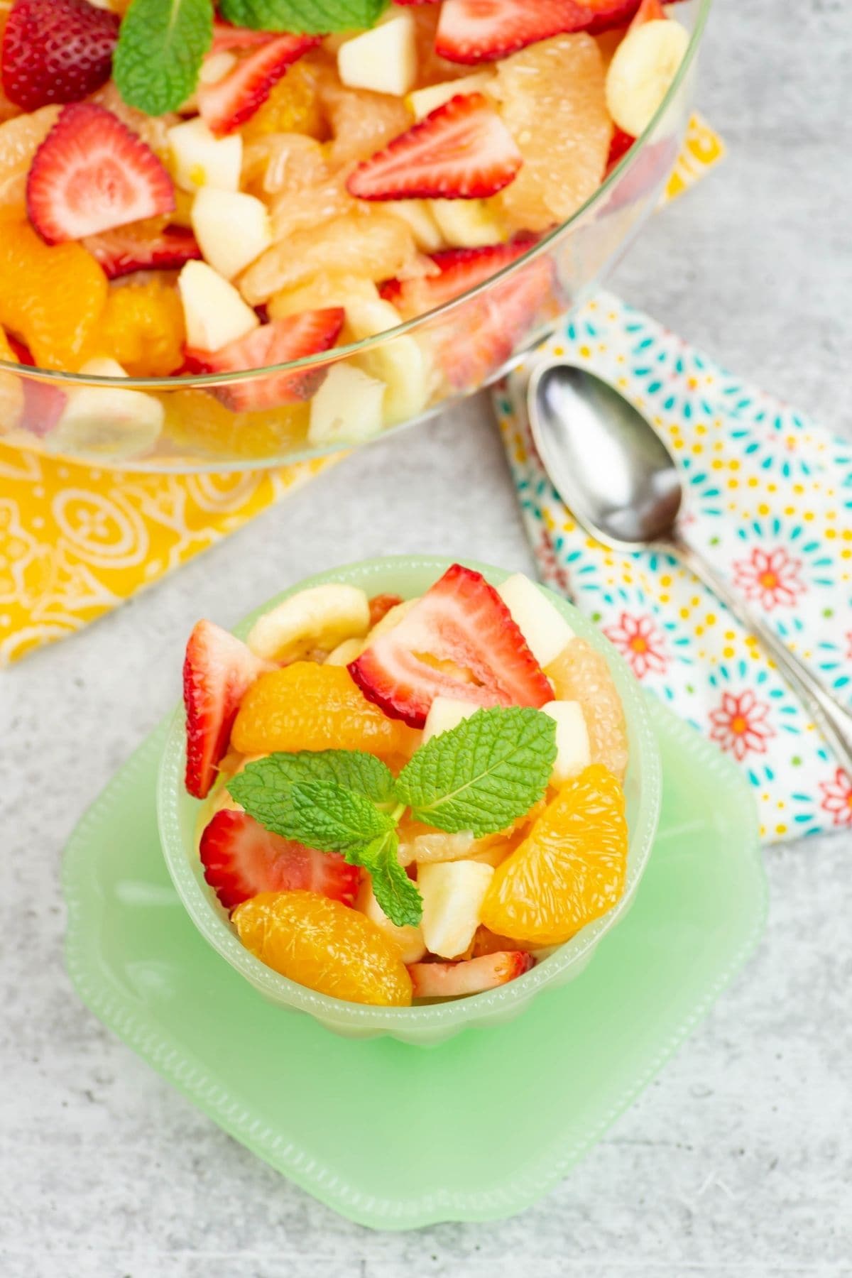 Long vertical image of a bowl with and a single serving bowl filled with fruit salad.