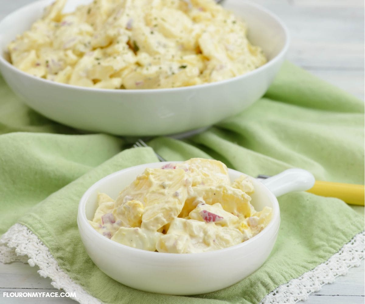 A small serving dish of potato salad with a larger serving bowl in the background.