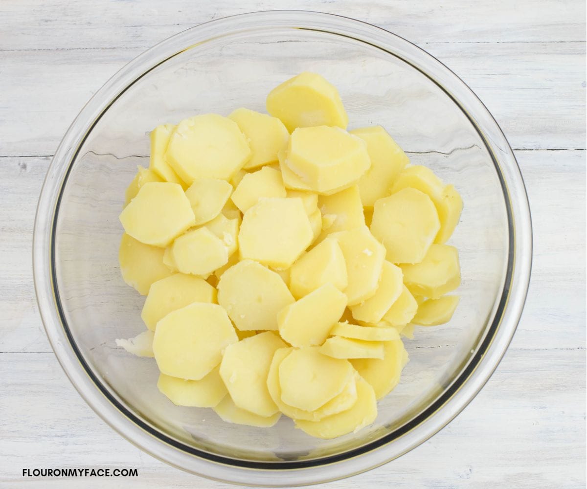 Sliced cooked yellow potatoes in a glass bowl.