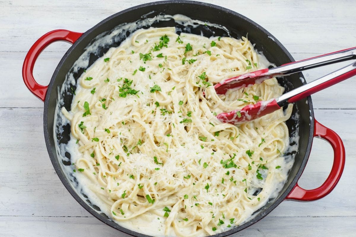 Fettuccine Alfredo garnished with parsley in a red skillet.