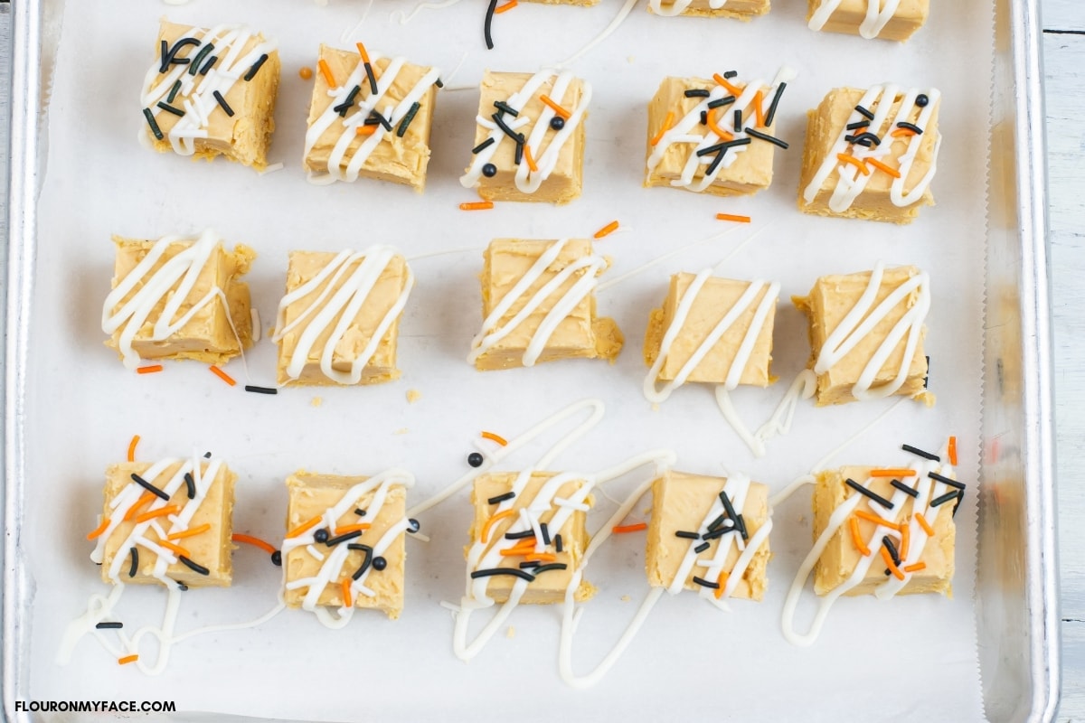 Pumpkin fudge squares decorated with melted chocolate and sprinkles on a parchment paper lined baking sheet as the chocolate hardens