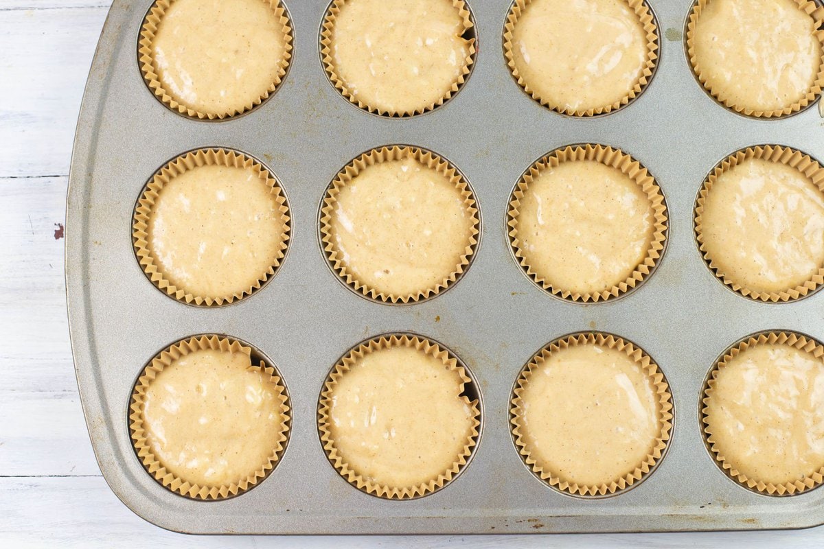 Closeup image of a muffin tin lined with parchment papers filled with banana muffin batter.