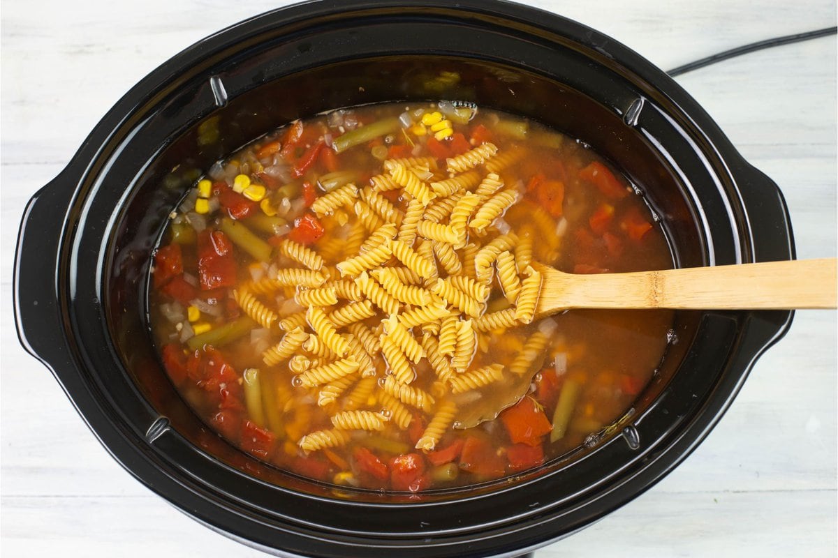 Overhead image showing uncooked pasta added to the vegetable soup.
