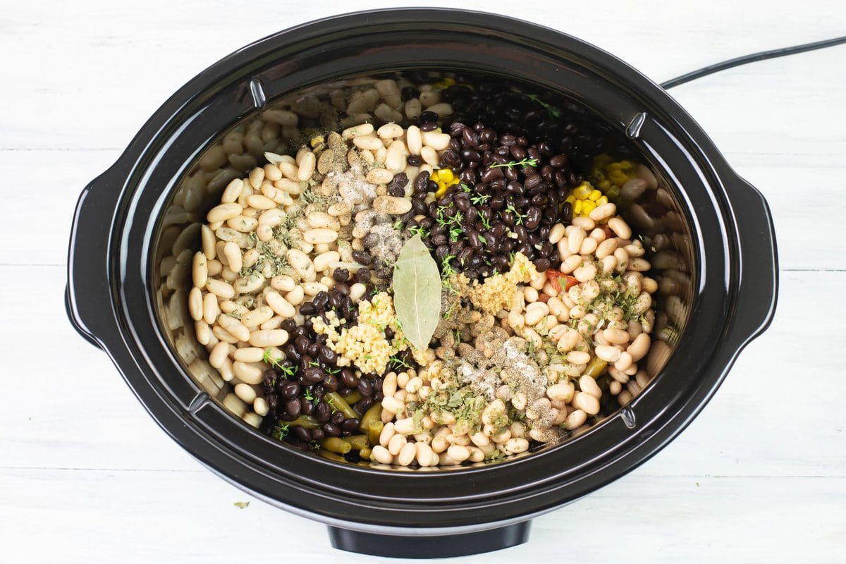Canned vegetables and beans, herbs and spices in a crock pot for soup recipe.