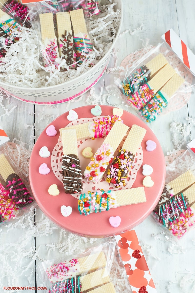 Decorated wafer cookies on a cake stand and in treat bags on a table.