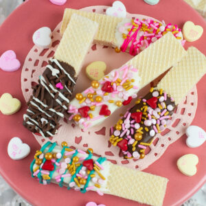 Valentines Day Chocolate Dipped Wafer Cookies on a pink cake stand with a pink doilie with conversation hearts