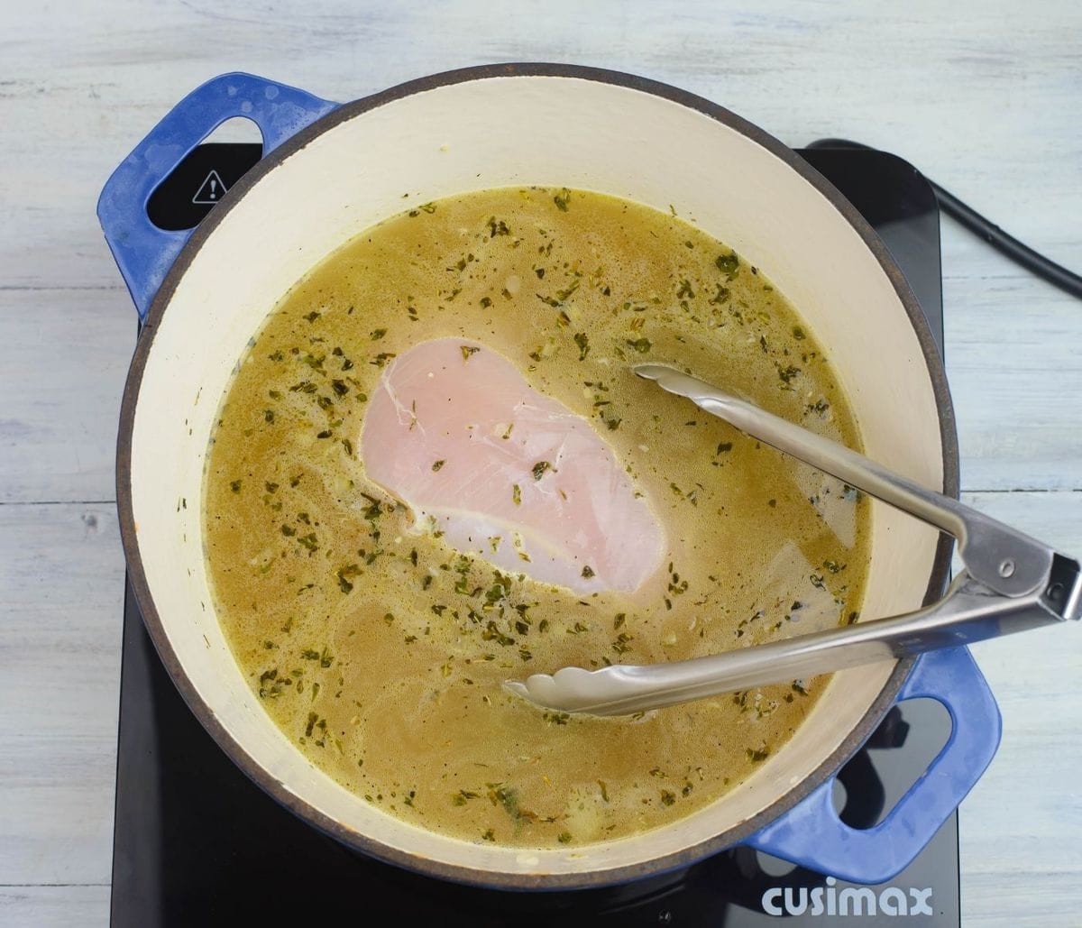 A chicken breast in the pot with chicken broth.
