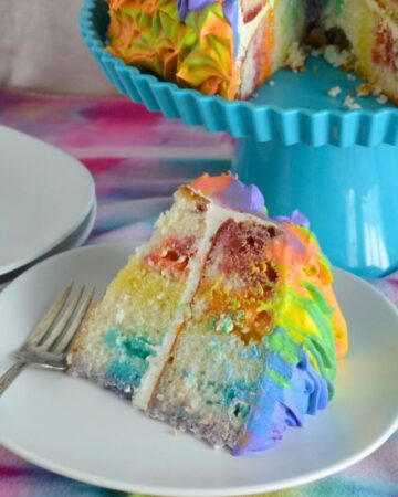 A thick slice of rainbow poke cake served on a plate.