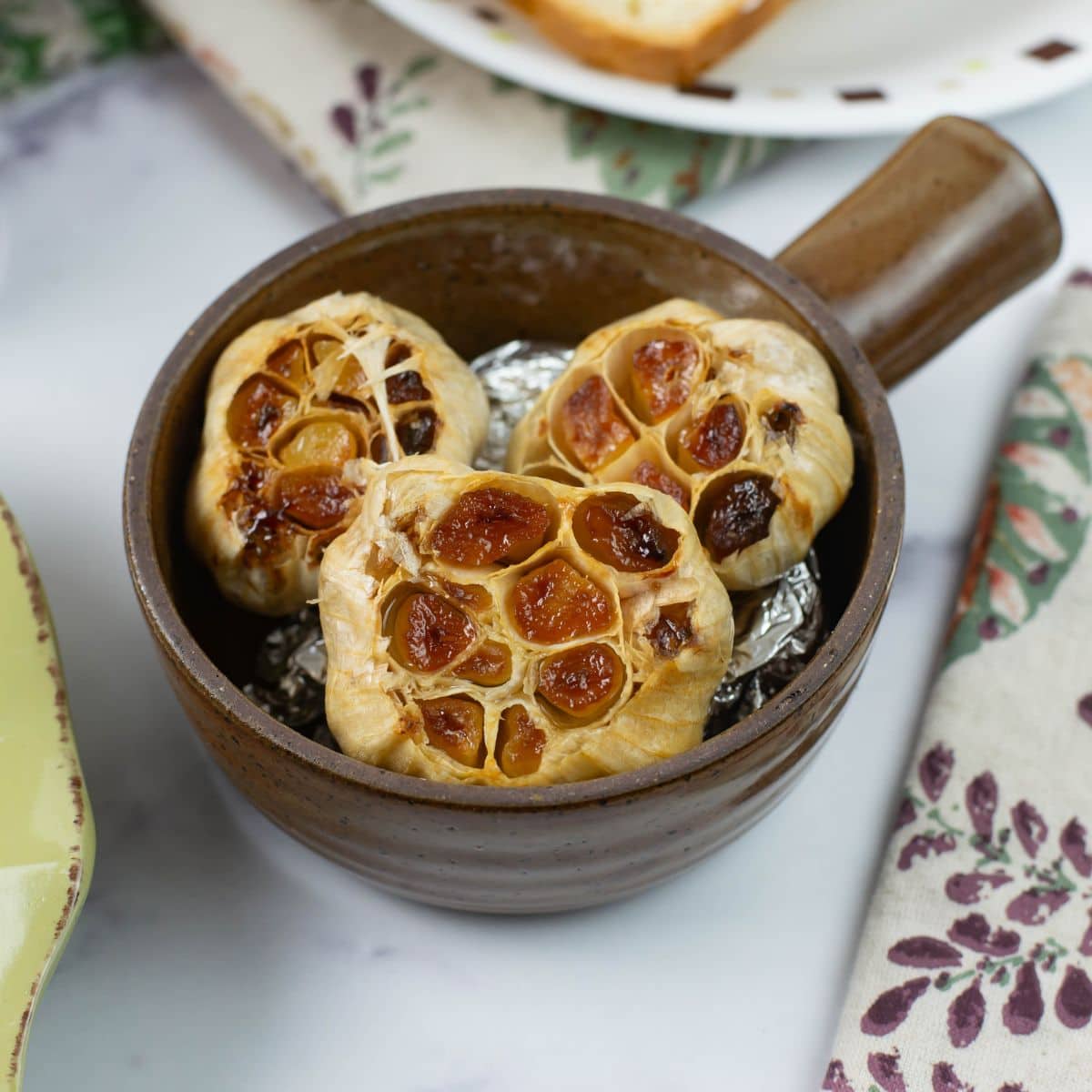 Three heads of roasted garlic in a stoneware bowl.