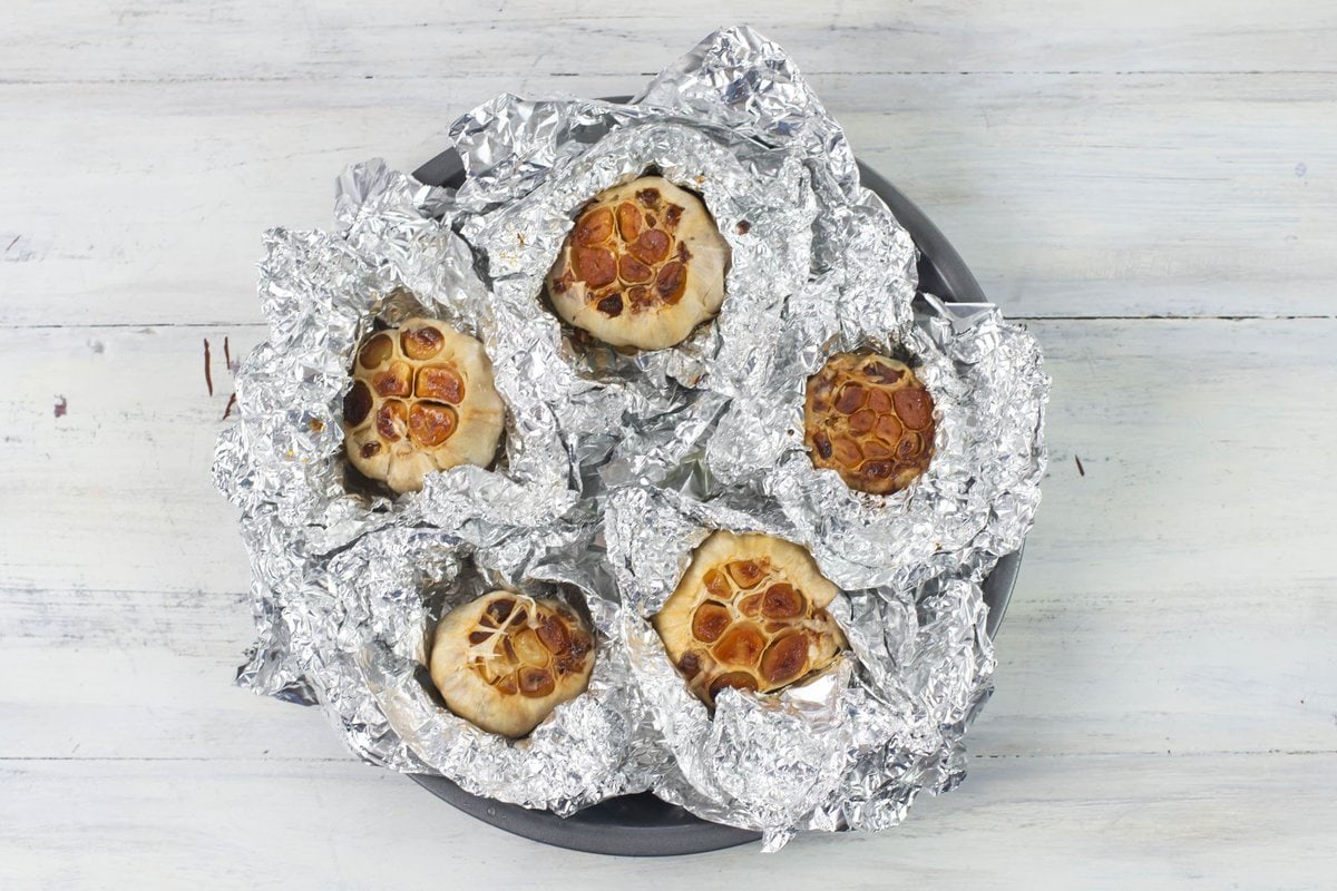 Roasted garlic aluminum bundles hot from the oven in a shallow pan.