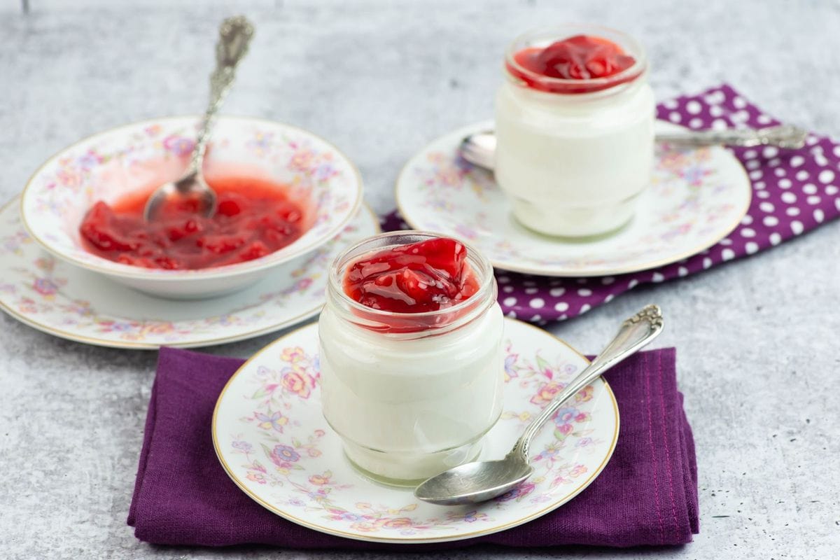 Two jars of homemade vanilla yogurt with a strawberry sauce topping.