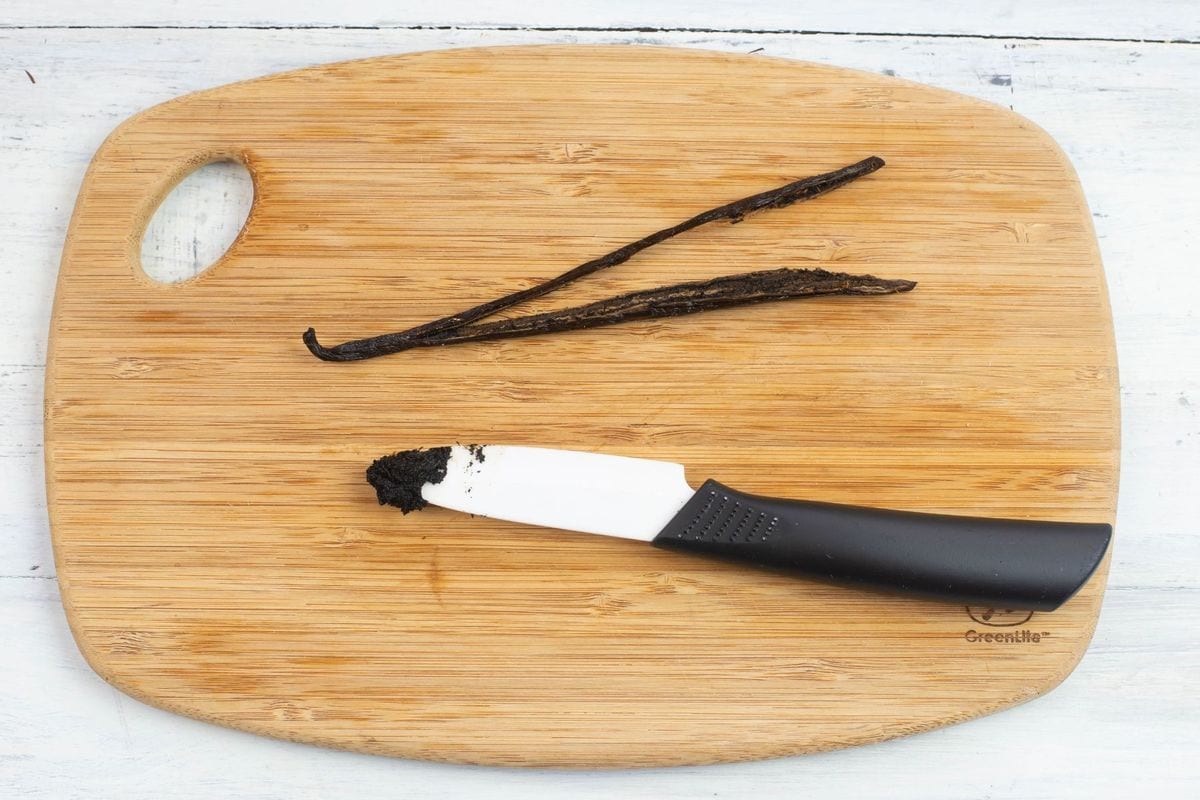 A split vanilla bean and small knife on a wooden cutting board.