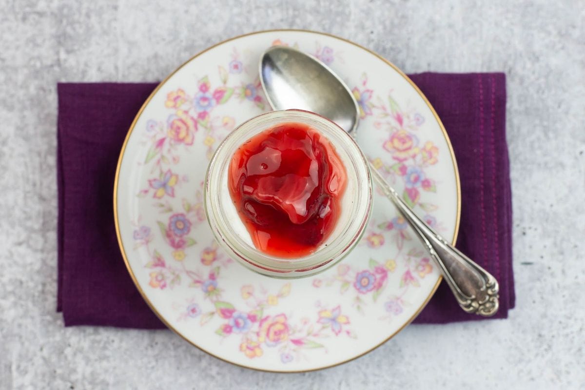 An overhead image of a small jar of vanilla yogurt topped with strawberry sauce.
