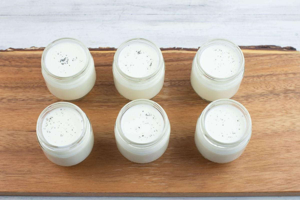 Six small jars filled with cultured milk on a wooden board.