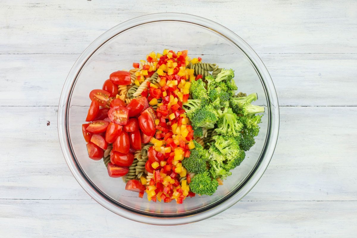 Tri-colored pasta, sliced cherry tomatoes, broccoli and diced bell peppers in a large bowl.