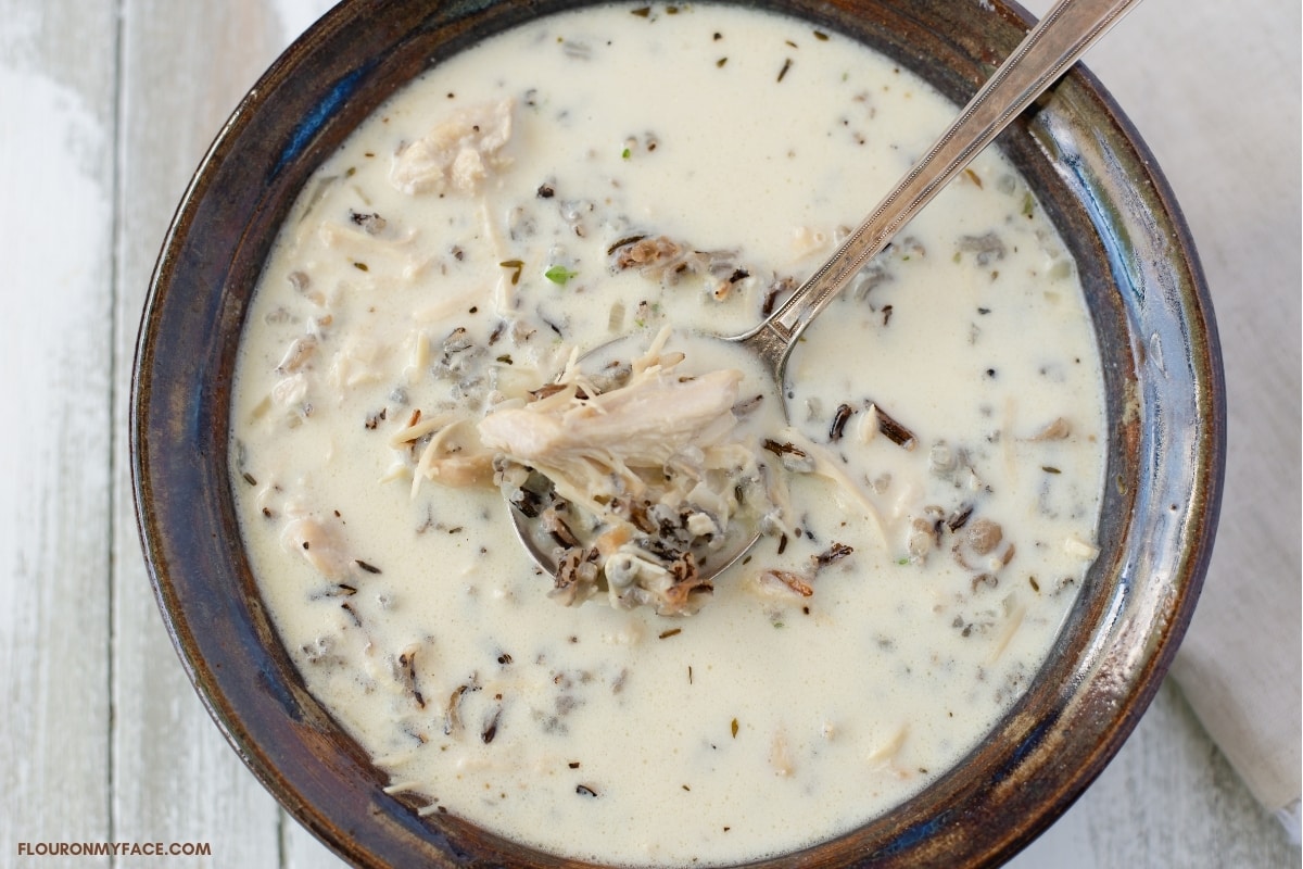 A brown glass bowl filled with a creamy chicken and wild rice soup