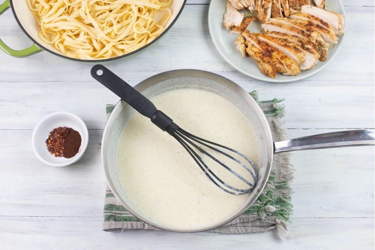 Homemade alfredo sauce in a skillet before mixing with pasta and Cajun chicken.