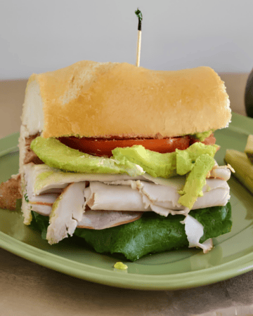 Club sub sandwich on a plate with sliced avocado.
