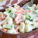 broccoli florets, cauliflower and carrots covered in a rich cream sauce in a serving tray.