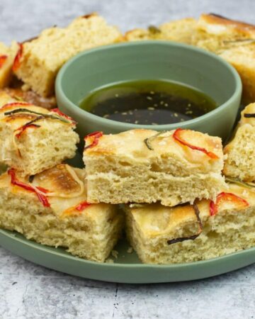 Sourdough Focaccia cut into pieces on a plate with a bowl of dipping oil.