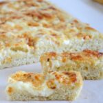 Onion Cheddar Focacci bread cut into pieces for an easy appetizer on parchment paper.
