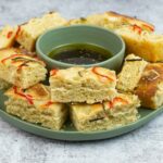 Sourdough Focaccia cut into pieces on a plate with a bowl of dipping oil.
