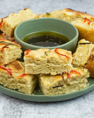 Sourdough Focaccia cut into pieces on a plate with a bowl of dipping oil.