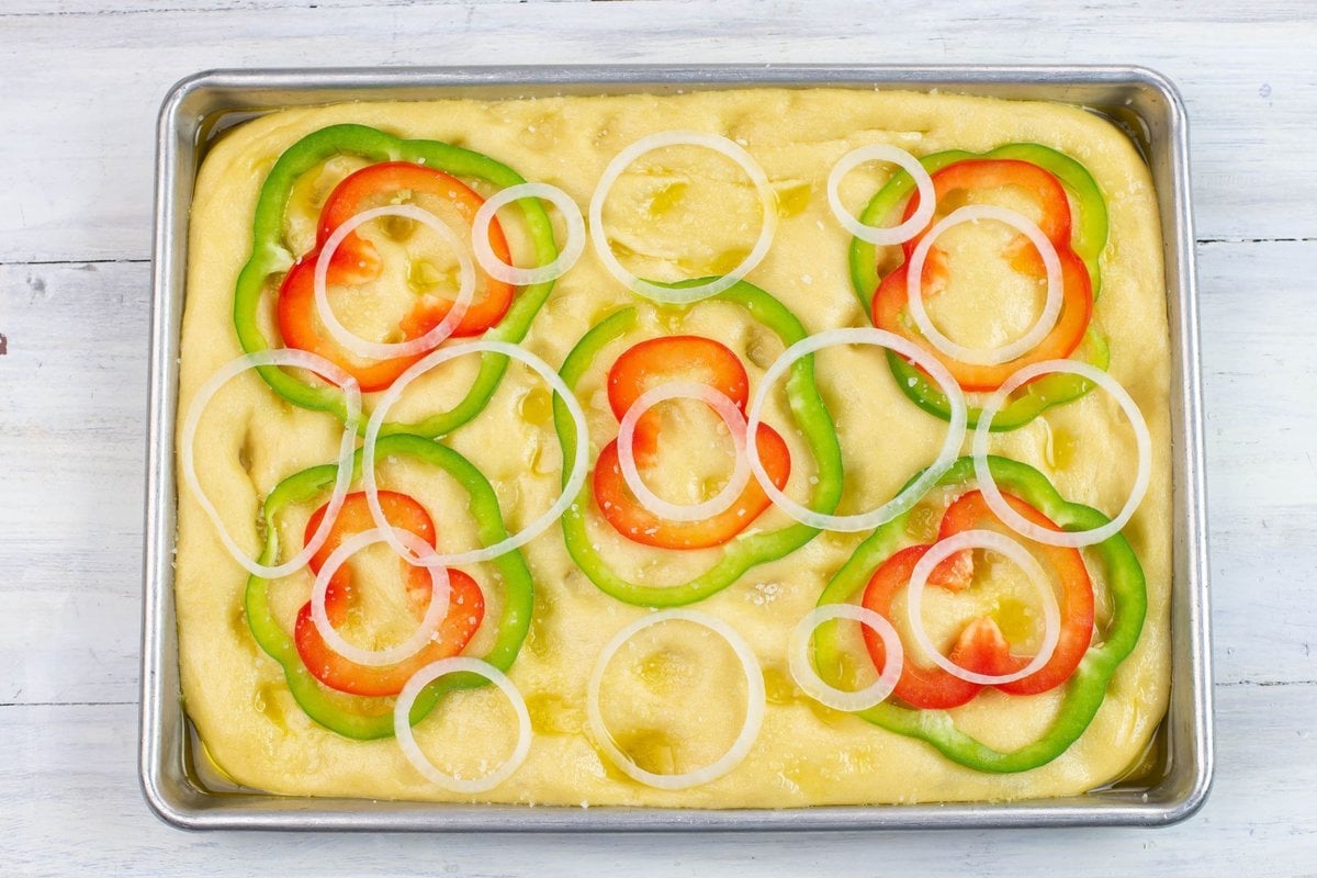 Topping focaccia with sliced onion and peppers before baking.