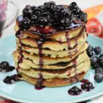 A tall stack of homemade buttermilk pancakes covered in blueberry syrup on a plate.