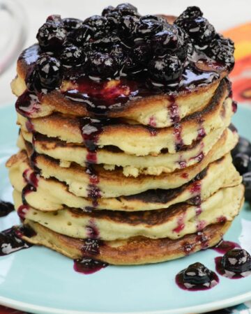A tall stack of homemade buttermilk pancakes covered in blueberry syrup on a plate.