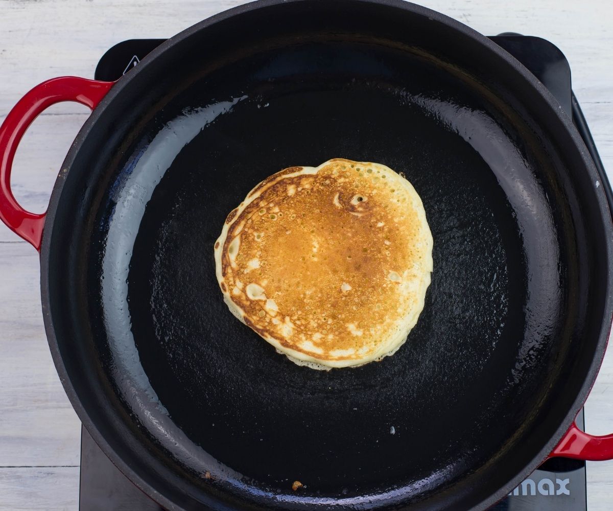 A golden brown pancake in the center of a hot skillet.