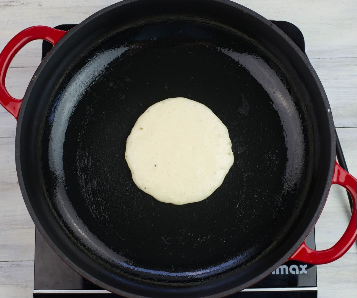 A ¼ cup scoop of pancake batter in the center of a skillet.