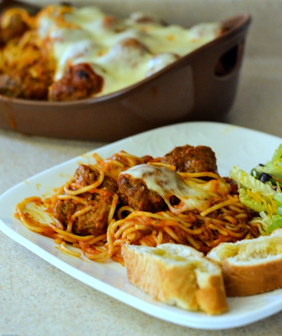 A small dinner plate with a serving of baked spaghetti with meatballs.  