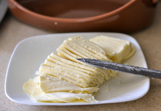 A block of fresh mozzarella cheese cut into thin slices on a plate.