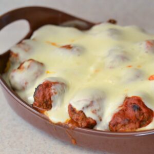Oval baking pan with baked spaghetti and meatballs topped with melted mozzarella cheese.
