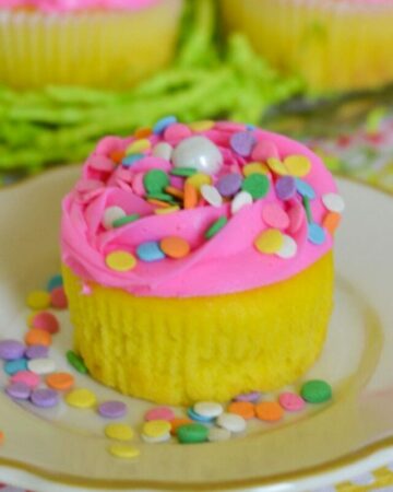 Yellow Easter cupcakes with pink frosting and confetti sprinkles on a plate.