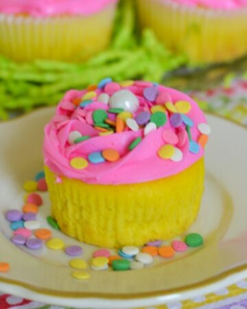 Yellow Easter cupcakes with pink frosting and confetti sprinkles on a plate.