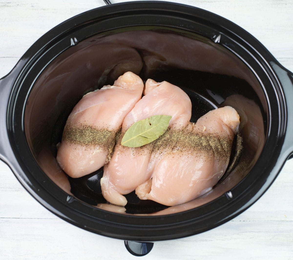 Boneless chicken, salt, pepper and bay leaves in a crock pot.