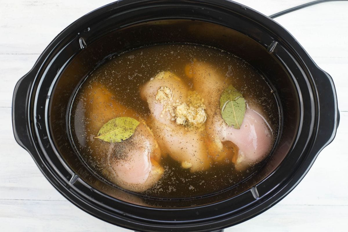 Boneless chicken with seasonings and broth in a crock pot.