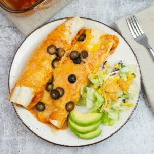 A dinner plate with a serving of chicken enchiladas, a salad and sliced avocado.