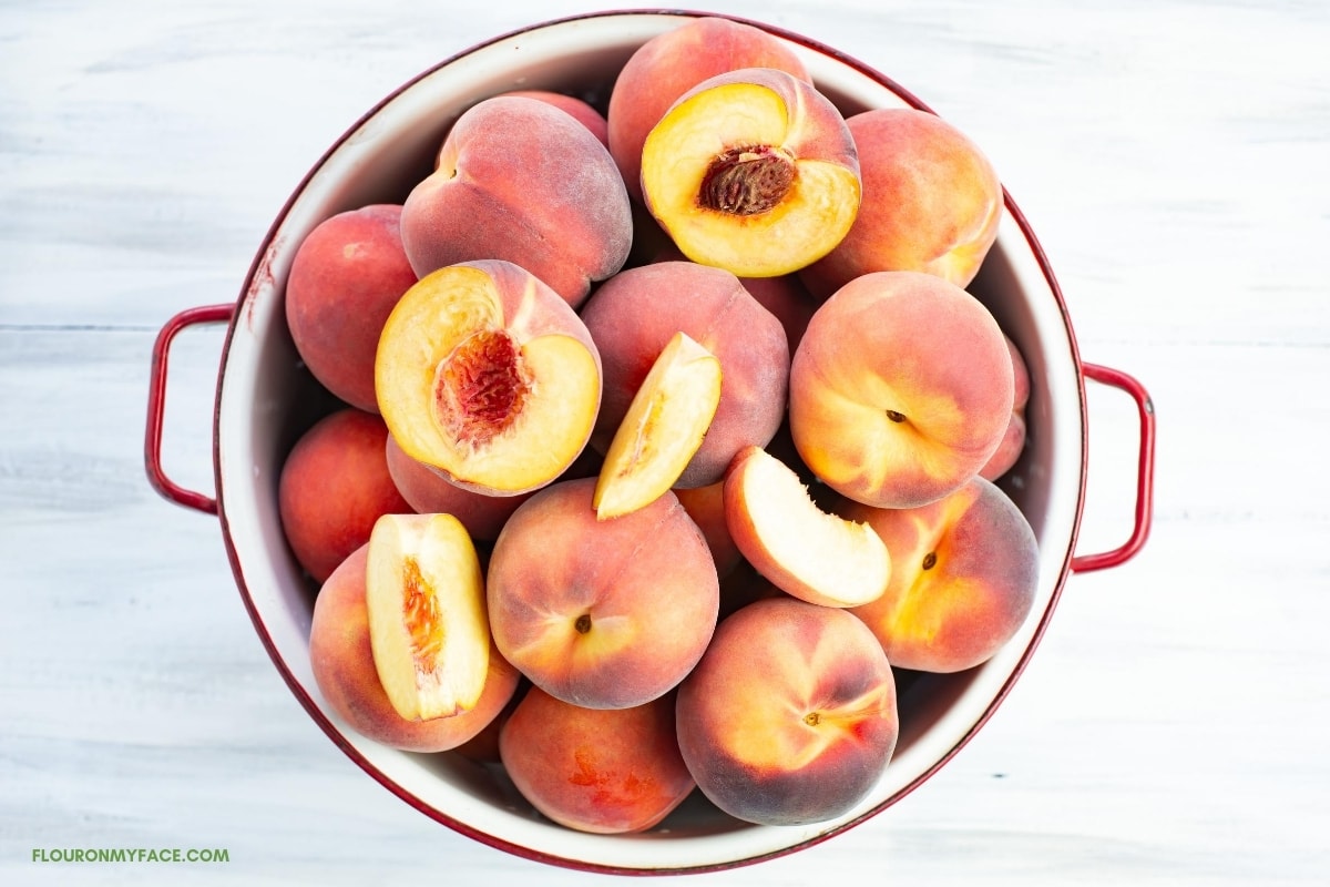 fresh whole and sliced peaches in a white enamel colander