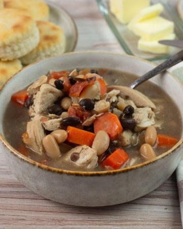 Bowl of chicken soup with biscuits in background.