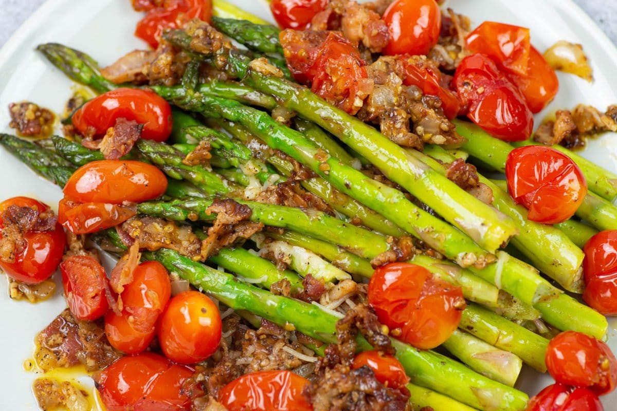 Closeup image of cooked asparagus spears on a bed of cooked grape tomatoes seasoned with bacon.